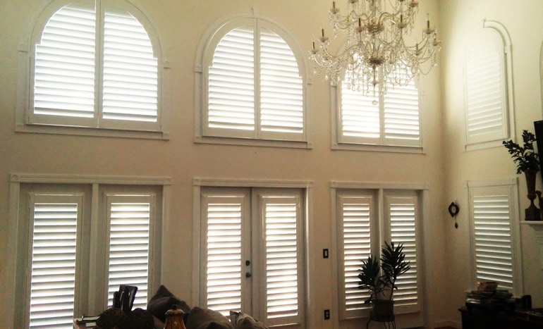TV room in two-story Fort Lauderdale house with plantation shutters on arch windows.